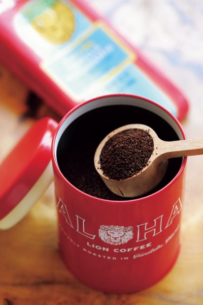 「A|LOHA」のロゴ入りキャニスター缶から、ライオンコーヒー一杯をスプーンで取り出す様子。