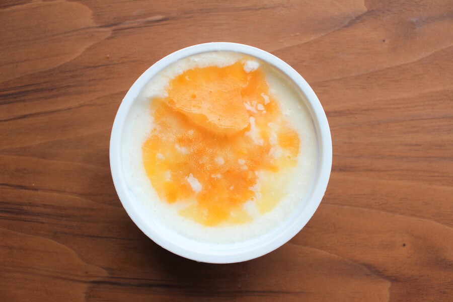 「7プレミアム　ピーチヨーグルト味氷」の蓋を開け、アイスの上部を撮影。果肉入りの桃ソースがかかっています。
