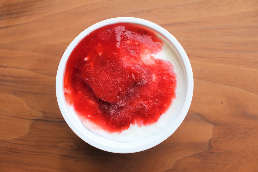 「7プレミアム　いちご練乳氷」の蓋を開け、アイスの上部を撮影。果肉入りのいちごソースがかかっています。