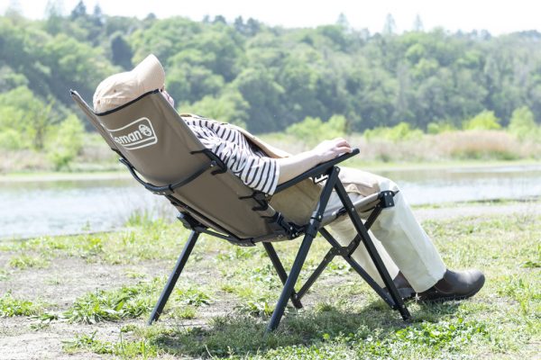 川のそばのキャンプ場に置かれたコールマンのチェアをリクライニングして寝る人