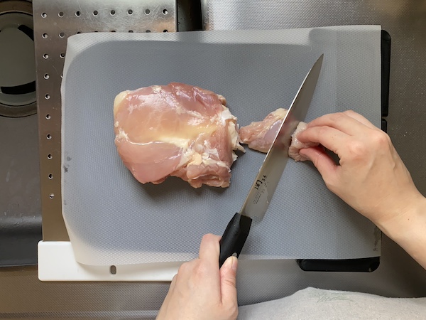 まな板に、まな板シートを敷いて、鶏肉を切っている様子。